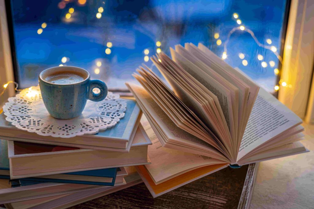 a photo of a Coffee cup, open book, fairy lights on window sill