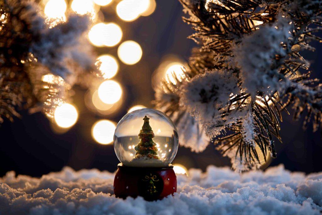 decorative christmas tree in snowglobe standing in snow with spruce branches and blurred lights at